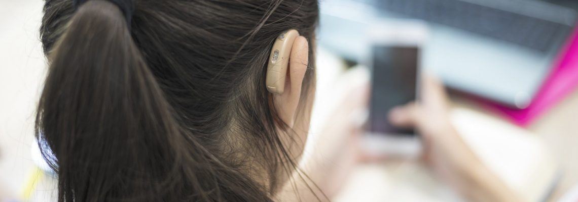 Young woman reading a phone screen while using a hearing-aid device